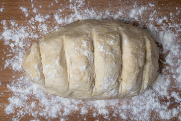 Raw dough covered with flour on a wooden cutting board.