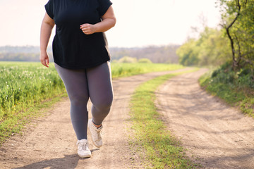Fototapeta na wymiar Young overweight woman running in nature. Female jogger doing morning physical training. Outdoor sports, activity, healthy lifestyle and weight loss