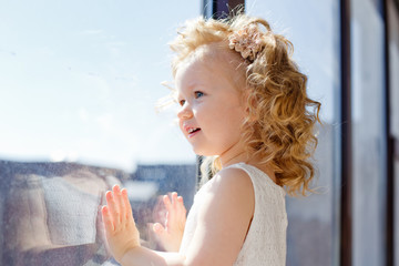 little girl dreamily looks out the window. the sun illuminates her face, flare. the child is on...
