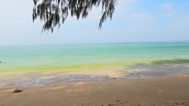 Tropical beach with white sand and turquoise sea at Koh Lanta island, Thailand. Relaxation on tropical paradise, view from shadow of tree. Vacation near waves from sea.