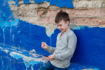 A teenage American boy carefully reads an article on the Internet from a smartphone. The child is sitting on the blue wall, smiling and happy.