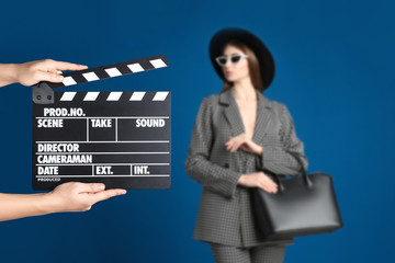 Assistant holding clapperboard and beautiful young woman on blue background, closeup. Cinema...