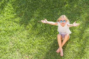 Summertime fun. cheerful girl in sunglasses sitting on the grass in the park. child outdoors. vacation in the summer park. top view