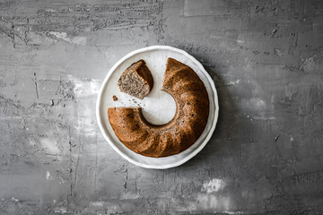 A poppy seed bundt cake on white ceramic plate on grey background, top view photo, copy space