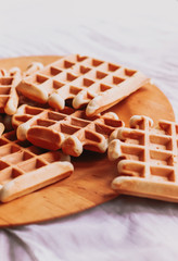 Belgian waffles on wooden plate on a white tablecloth. Eating at home