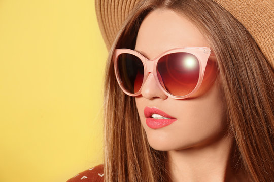 Young woman wearing stylish sunglasses and hat on yellow background