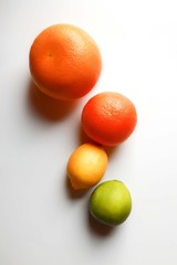 Four citrus fruits on white surface: grapefruit, orange, lemon and lime. Top view. Unripped.