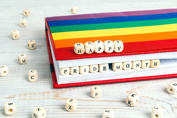 Happy pride month written in wooden blocks in red notebook with rainbow LGBT flag on wooden table.