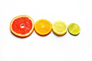 Four different sized slices of citrus fruits: grapefruit, orange, lemon and lime. Placed in order from largest to smallest.