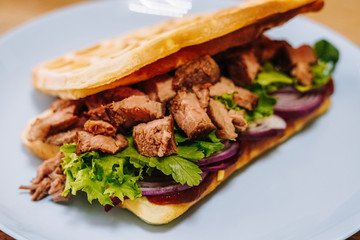 tasty Belgium waffle with lettuce, meat, egg and vegetables served of pretty blue plate