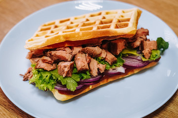 tasty Belgium waffle with lettuce, meat, egg and vegetables served of pretty blue plate