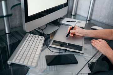 Workplace of photographer or graphic designer. Creative designer hands working on laptop with graphic tablet. Computer monitor, keyboard, empty notebook, mouse, smartphone