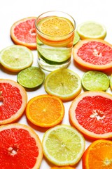 Glass of water standing among assorted slices of citrus fruits: grapefruit, orange, lemon, lime.