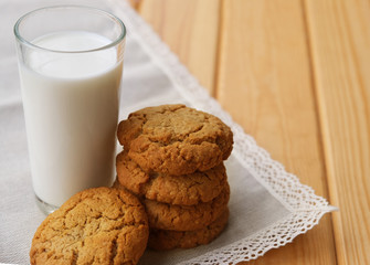 homemade oatmeal cookies tied with thread on a natural linen napkin with lace, next to glass of milk. It lies on a light wooden background. rustic style