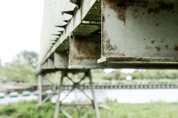 Shallow focus, high contrast of a weathered metal conveyor system, spanning a river. The paintwork is seen weathered in this industrial view.