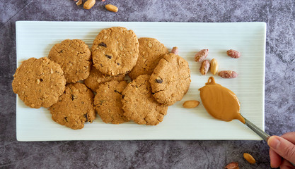 Top view on a bunch of peanut butter cookies in white plate and a spoon of natural peanut butter,...