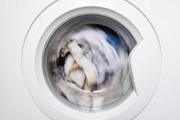 Laundry washing clothes rotating in machine drum front view.