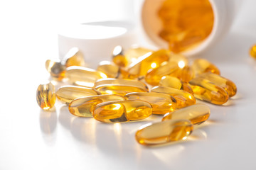 Cod liver oil capsules scattered from a bottle on white background