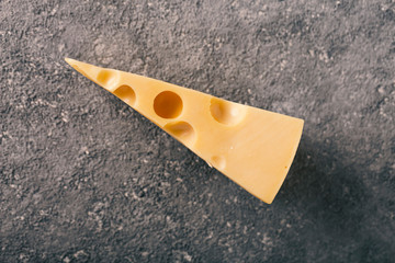 Piece Maasdam cheese on concrete gray background.