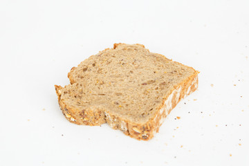 Single sliced piece of cereal bread and crumbs. Delicious crusty loaf toast isolated on white background. Studio shot. Angled view. Homemade bakery and nutrition concept
