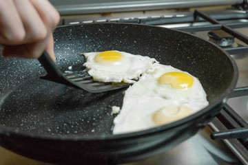 woman's hand using a black spatula takes a fried egg from the pan