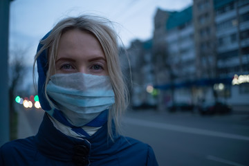 young blonde woman with a stole on her head in a medical mask close-up on a street in the city. Prevention of the spread of the flu virus.