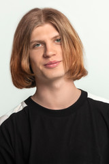 Close up portrait of young handsome guy with red ginger hear, slightly smiling, looking right to the camera. Wearing casual black shirt. Light gray background, studio, copy space.