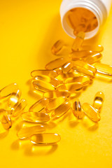 Fototapeta na wymiar Yellow capsules scattered from a white bottle on orange background