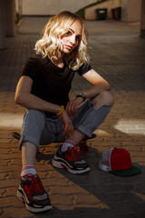 A young blonde girl sits on a skateboard in the beam of light, offended by her boyfriend. Dressed in a black T-shirt with short ripped jeans and sneakers.