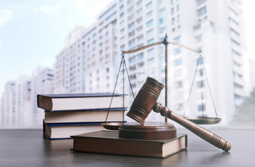 Wooden gavel, scales of justice and books on table against beautiful cityscape