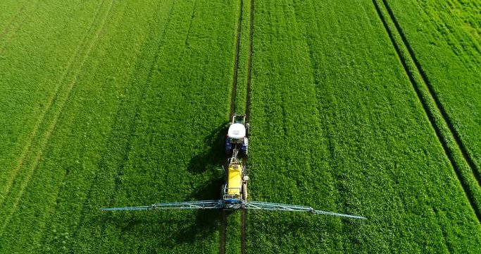 Drone follow shot of a tractor spraying pesticides on green field with sprayer at spring. Fertilization agriculture, fertilizer application by field mechanization.