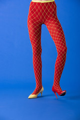 cropped view of model in fishnet tights, yellow and red heels standing on blue