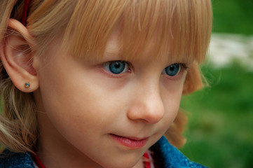 Cute little girl with curly blond hair in a park on a summer day. Close-up portrait of a blue-eyed girl.