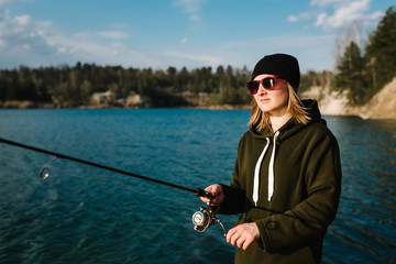 Woman catching a fish, pulling rod while fishing on lake or pond at the weekend. Fisherman with rod, spinning reel on the river bank. Sunrise. Fishing for pike, perch, carp. Background wild nature.