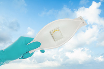 Hand holding protective mask on sky clouds background, safety and virus protection concept