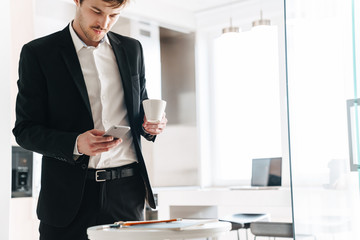 Photo of serious businessman drinking coffee and using cellphone