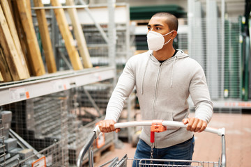Ein Mann kauft zur Zeit des Coronavirus in einem Baumarkt ein, er trägt eine Maske und schiebt einen Einkaufswagen  - obrazy, fototapety, plakaty
