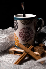 Taza de té con canela y azúcar moreno sobre tela blanca de rejilla y fondo negro