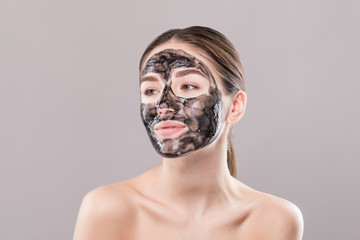 Young woman with purifying black mask on her face isolated on white background