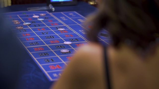 Luxury girl playing roulette. The dealer collects chips. Back view.