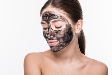 Young girl with a black cosmetic mask on her face holding a brush isolated on a white background