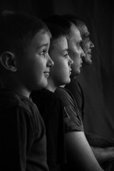 Two sons, father and grandfather in profile against a dark background. Two children and two adults of European race in profile on black and white photograph. Three male generations.