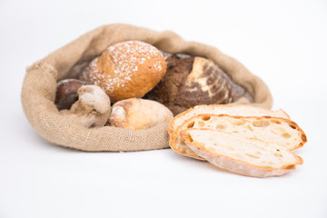 Closeup of sliced wheat bread and crusty homemade buns in rustic jute sack. Isolated object on white background. Baking or traditional bread concept