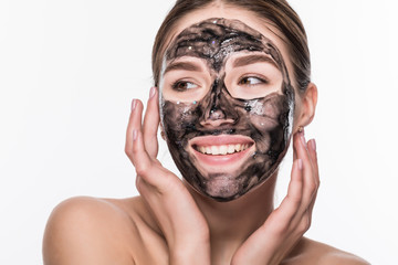 Young girl with a black cosmetic mask on her face holding a brush isolated on a white background