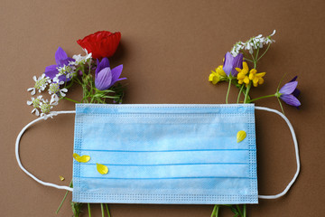Flat lay with blue medical mask and wildflowers on a brown background. Coronavirus Covid quarantin...