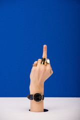 cropped view of woman with wristwatch on hand showing middle finger isolated on blue