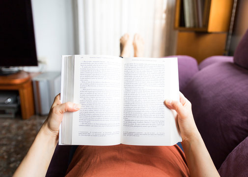 Mujer en cuarentena tumbada en el sof&aacute; leyendo un libro
