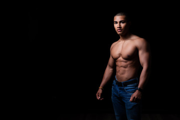 Fototapeta premium Attraktiver muskulöser junger Mann posiert mit angespannten Muskeln, Portrait vor schwarzem Hintergrund mit copy space 