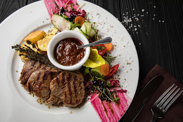Grilled fillet with vegetables and sauce on a dark background