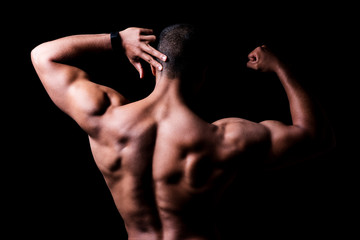 Obraz na płótnie Canvas Ein Mann mit muskulösem Rücken vor schwarzem Hintergrund, angespannte Rückenmuskulatur 
